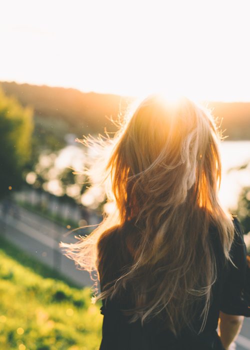 mujer de espaldas bajo una puesta de sol